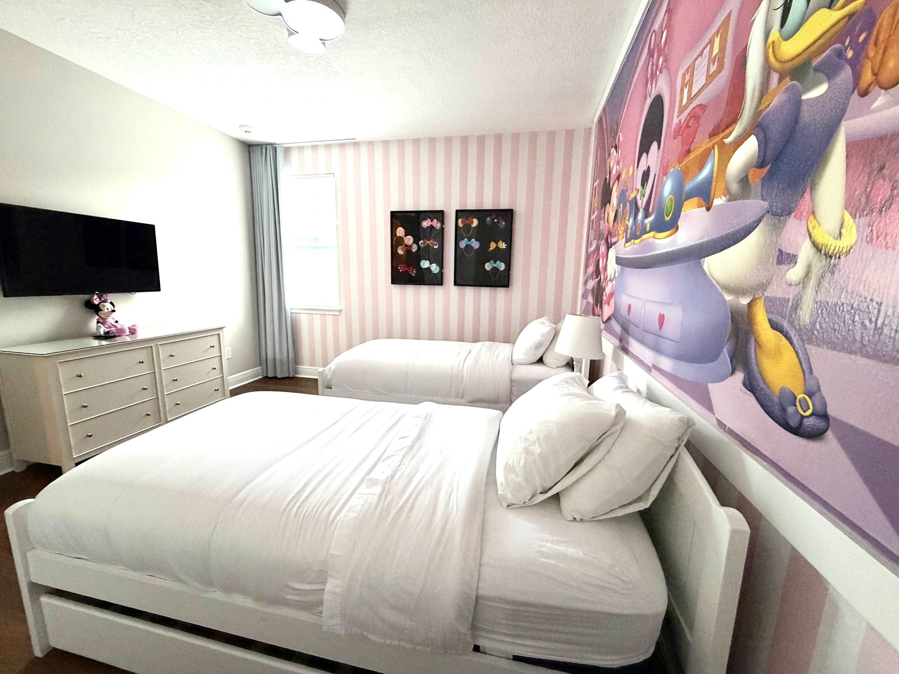 A bedroom with two beds, a flat-screen TV, a dresser, and a wall mural.