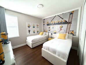 A bedroom with two beds, a window with blinds, and a wall decorated with minion-themed artwork. - Onyx Villa Luxury 12 Bed Home 9 Mins to Disney World (Kissimmee)