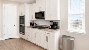 Una cucina con mobili bianchi, un forno a microonde, un forno, una macchina per il caffè e un cestino.