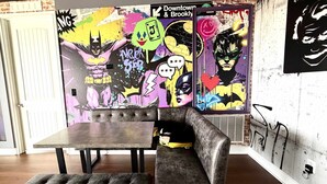 Una stanza con un divano in pelle marrone scuro, un poggiapiedi abbinato e un tavolino. Le pareti sono decorate con graffiti colorati.