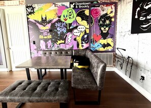 Ein Zimmer mit einem dunkelbraunen Ledersofa, einem passenden Hocker und einem kleinen Tisch. Die Wände sind mit farbenfroher Graffiti-Kunst gestaltet.
