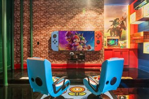 A gaming area with a large screen, two blue gaming chairs, and a brick wall. - The Premiere House - 8 Mins to Universal Studios 3 Mins to Sea World 15 Mins to Disney World (Orlando)