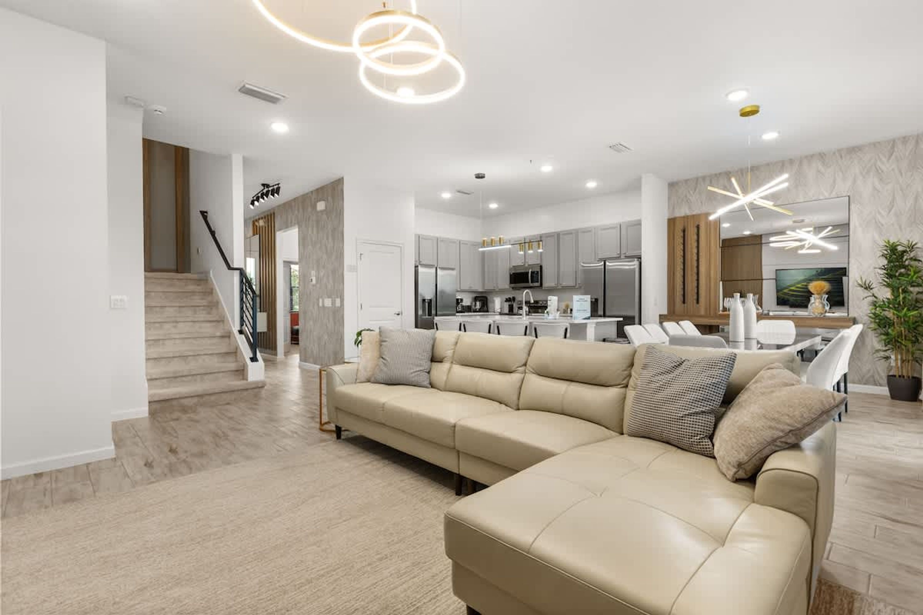A modern living room with a sectional sofa, a staircase, and a kitchen in the background.