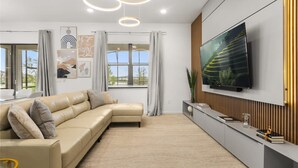 A modern living room with a sectional sofa, a flat-screen TV mounted on the wall, and a large window with curtains. - The Premiere House - 8 Mins to Universal Studios 3 Mins to Sea World 15 Mins to Disney World (Orlando)