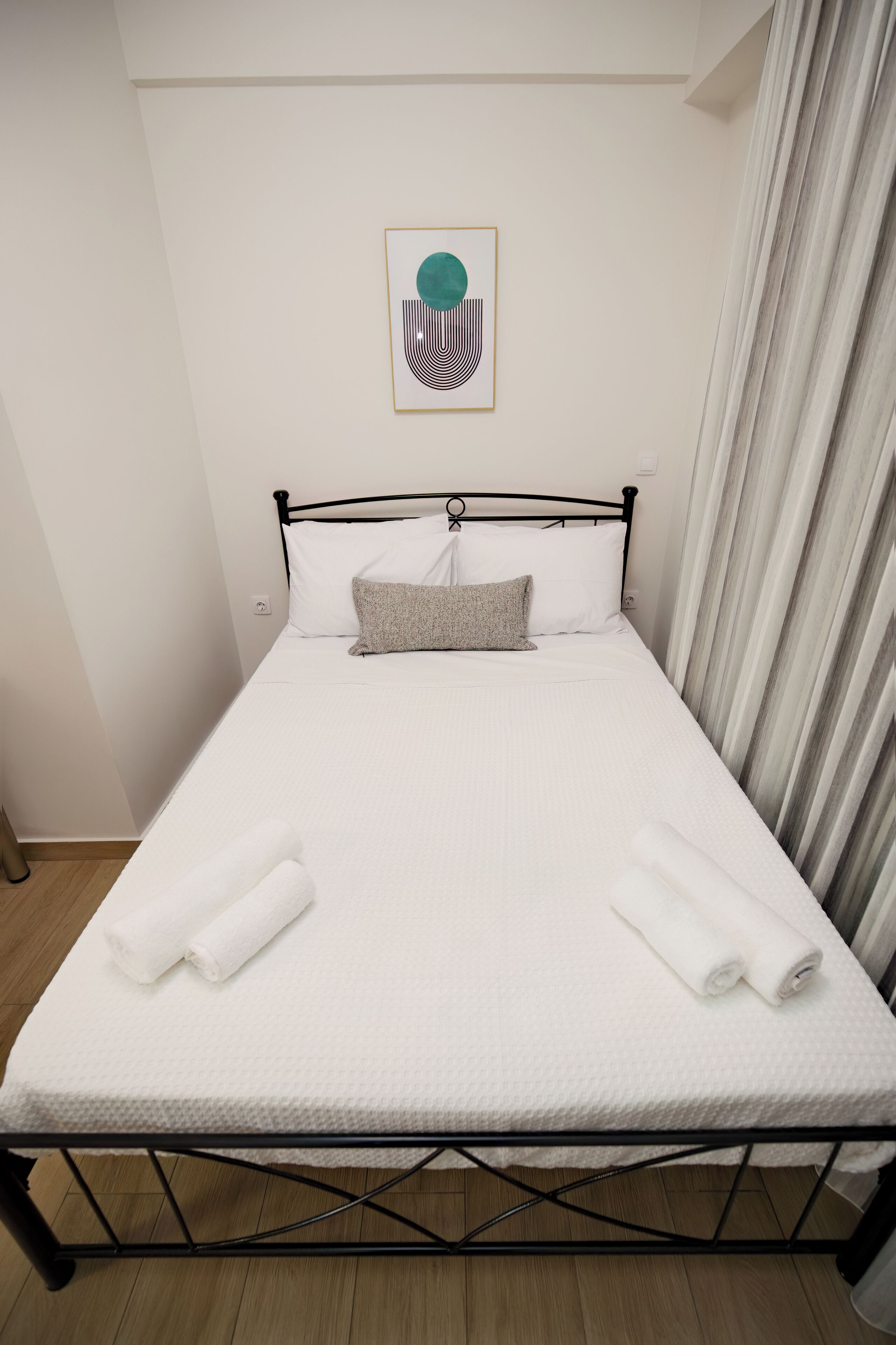 A single bed with white bedding, a grey pillow, and rolled towels.