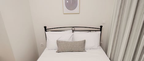 A single bed with white bedding, a grey pillow, and rolled towels.