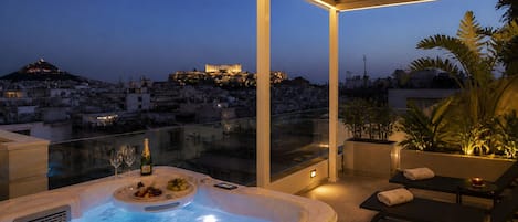Terraza en la azotea con jacuzzi, zona de estar y vistas a un paisaje urbano al anochecer.