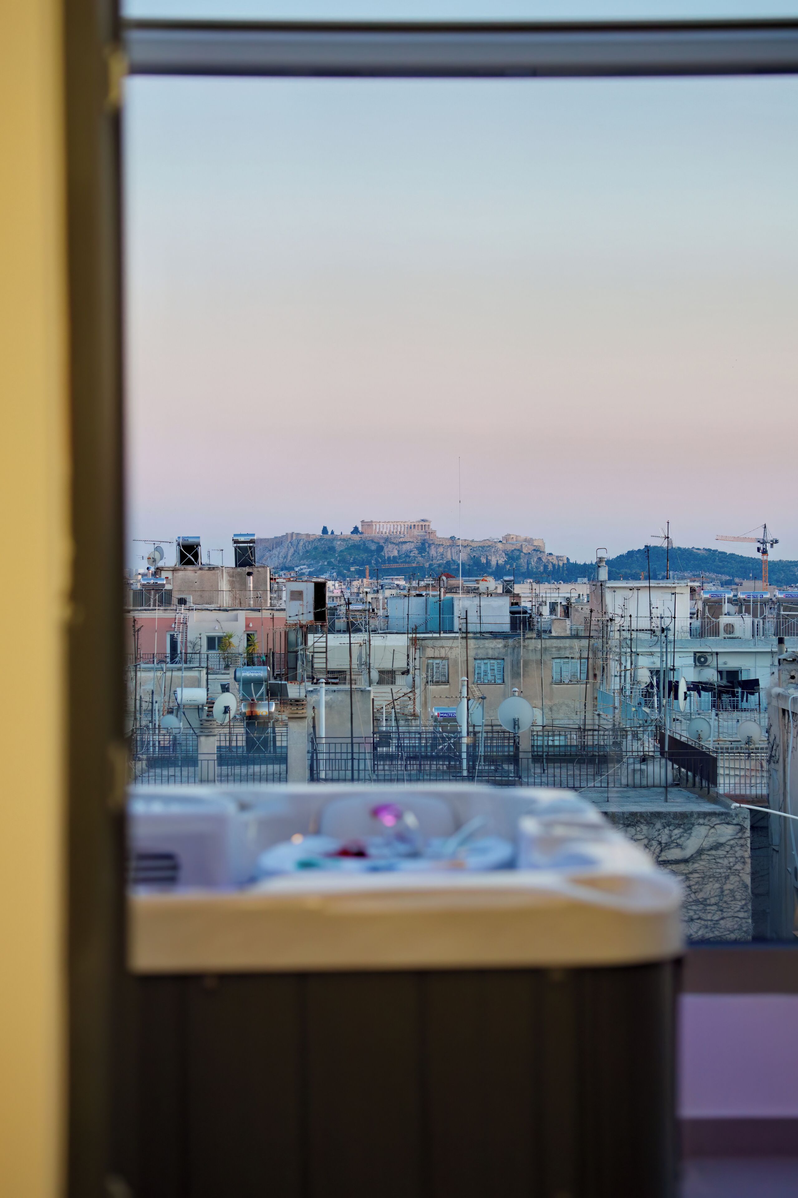 Une vue depuis une fenêtre donnant sur un paysage urbain, avec des bâtiments et une colline au loin.