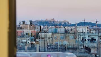Une vue depuis une fenêtre donnant sur un paysage urbain, avec des bâtiments et une colline au loin.