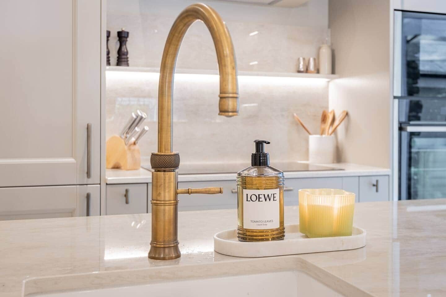 Une cuisine avec un robinet moderne, une bouteille de lotion et une bougie posée sur le comptoir.
