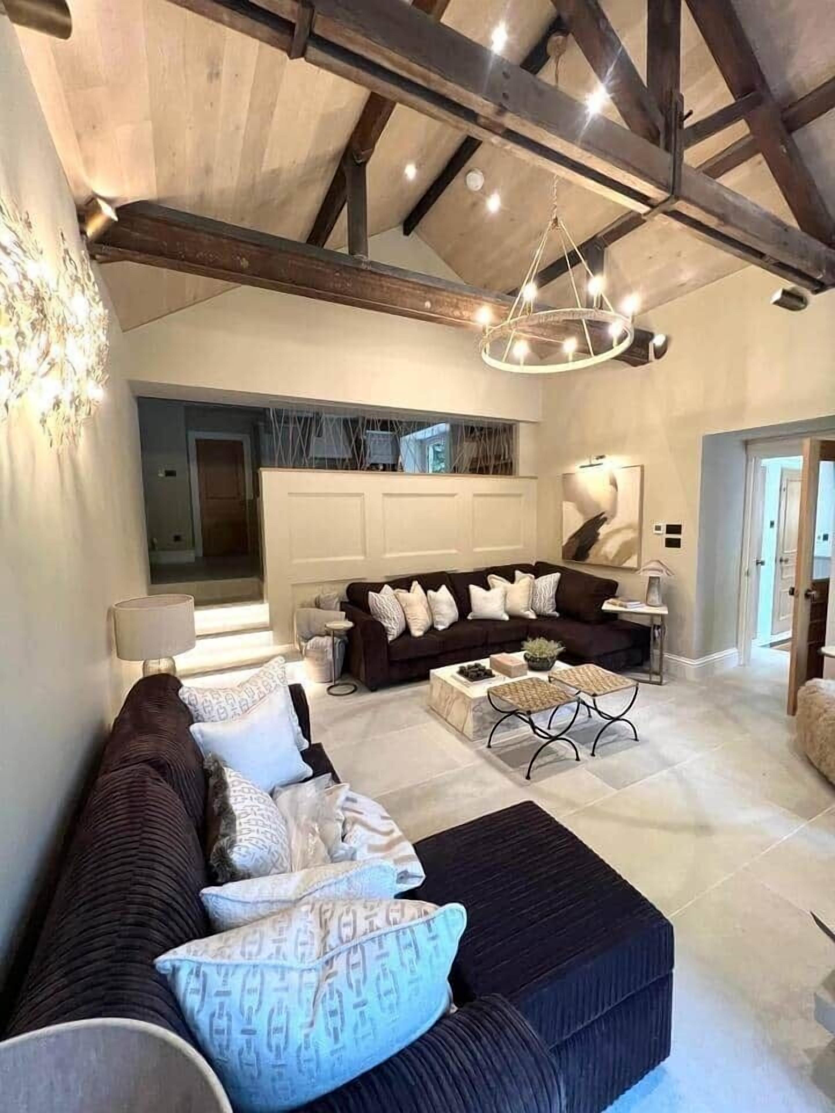A spacious living area with a dark-colored sofa set, a coffee table, and a chandelier.