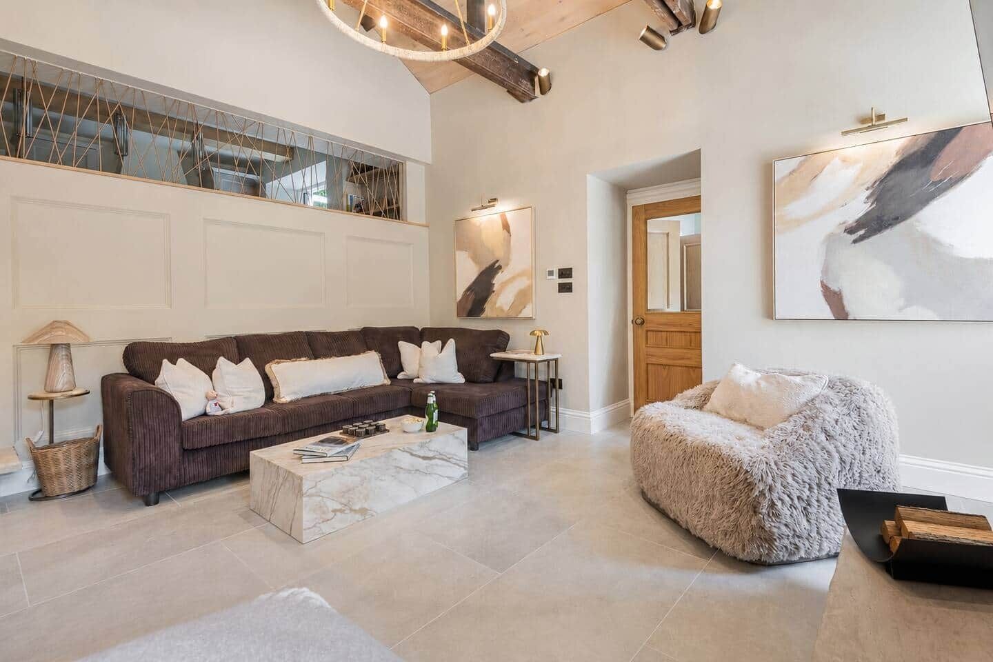 Un salon spacieux avec un grand canapé d’angle, une table basse ronde et un pouf moelleux.