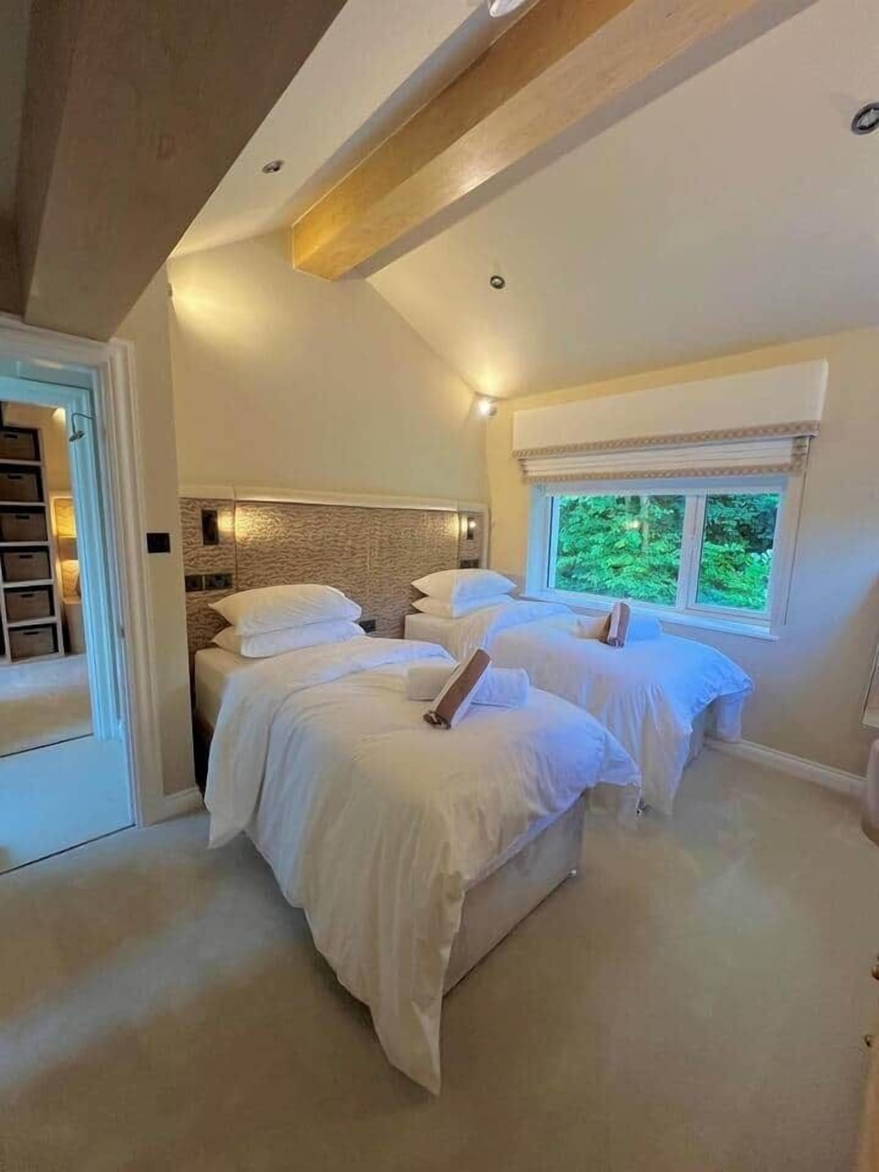 A bedroom with two beds, a wooden ceiling, and a window with a view of greenery.