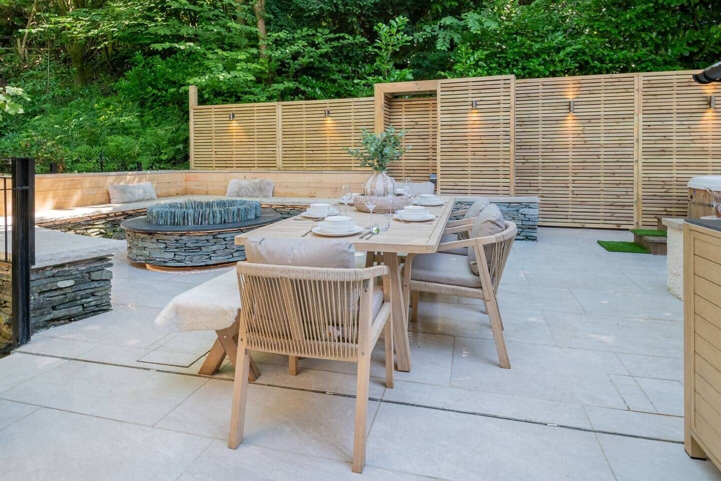 An outdoor patio with a stone fire pit, wooden furniture, and a dining table set for four.
