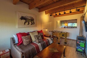 A cozy living room with a sofa, a foosball table, and a bear painting on the wall. - Heavenly Vista Lago Lake View - Luxury Ski-In-Ski-Out Retreat with Stunning Lake Views (Stateline)