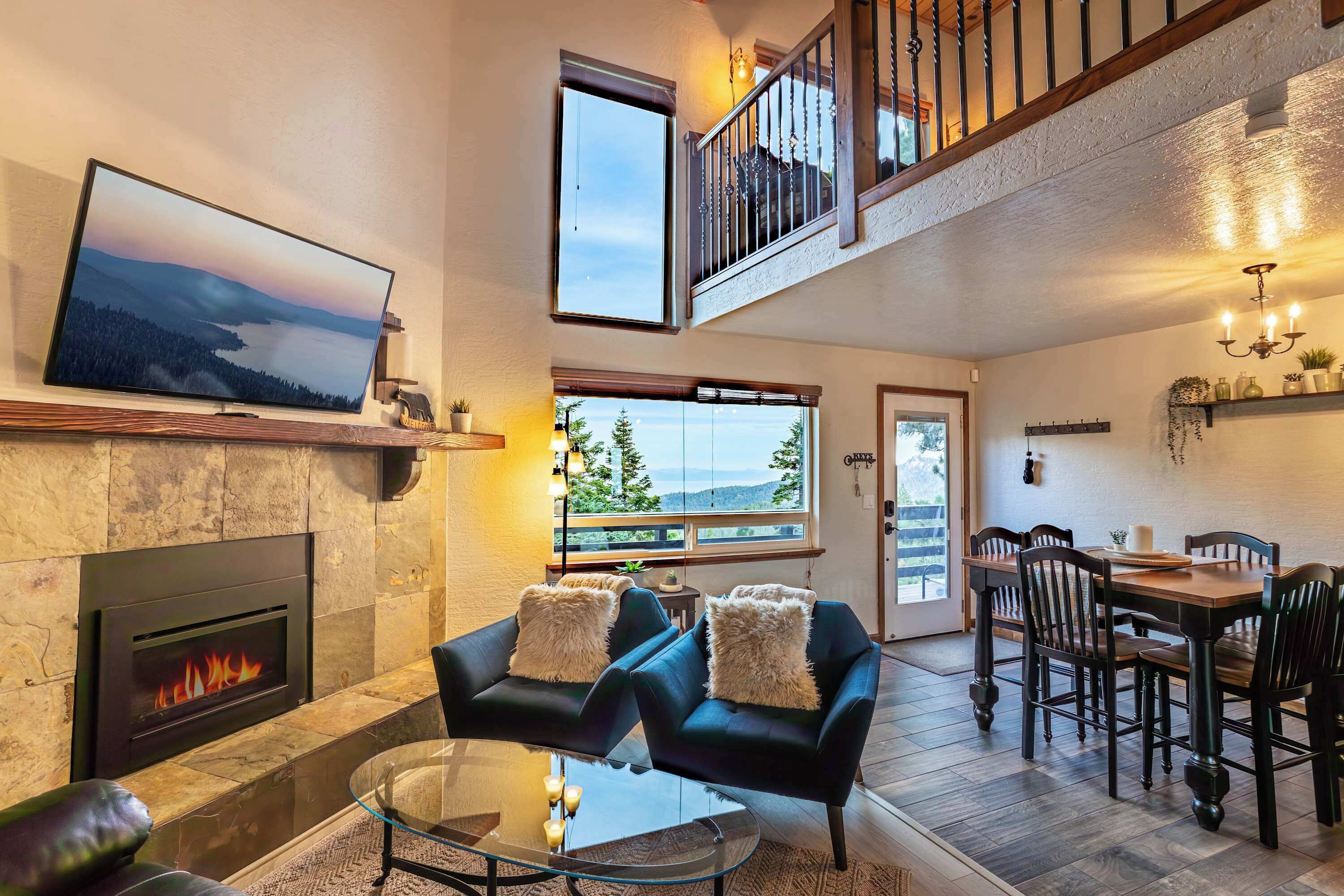 Un vaste espace de vie comprenant une cheminée, un téléviseur, une table à manger avec des chaises et un balcon offrant une vue agréable.