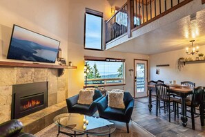 Amplia sala de estar con chimenea, televisor, mesa de comedor con sillas y balcón con vistas.