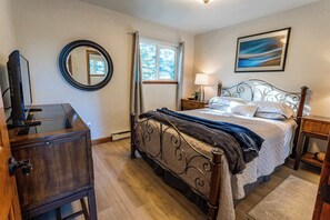 A bedroom with a bed, a bedside table, a lamp, a mirror, a window, and a painting on the wall. - Heavenly Vista Lago Lake View - Luxury Ski-In-Ski-Out Retreat with Stunning Lake Views (Stateline)