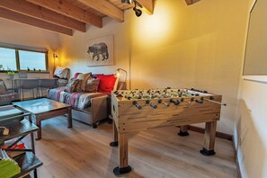 Una sala de estar acogedora con una mesa de fútbol de mesa, un sofá y una ventana con vista a un lago.