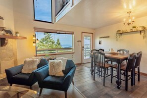 A modern interior with a dining area, two sofas, a chandelier, and a large window with a view. - Heavenly Vista Lago Lake View - Luxury Ski-In-Ski-Out Retreat with Stunning Lake Views (Stateline)