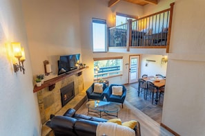 A spacious living area with a fireplace, a television, and a dining area with a table and chairs. - Heavenly Vista Lago Lake View - Luxury Ski-In-Ski-Out Retreat with Stunning Lake Views (Stateline)