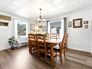 Une salle à manger avec une table et des chaises en bois, des murs blancs et un plafond orné d’un motif géométrique.