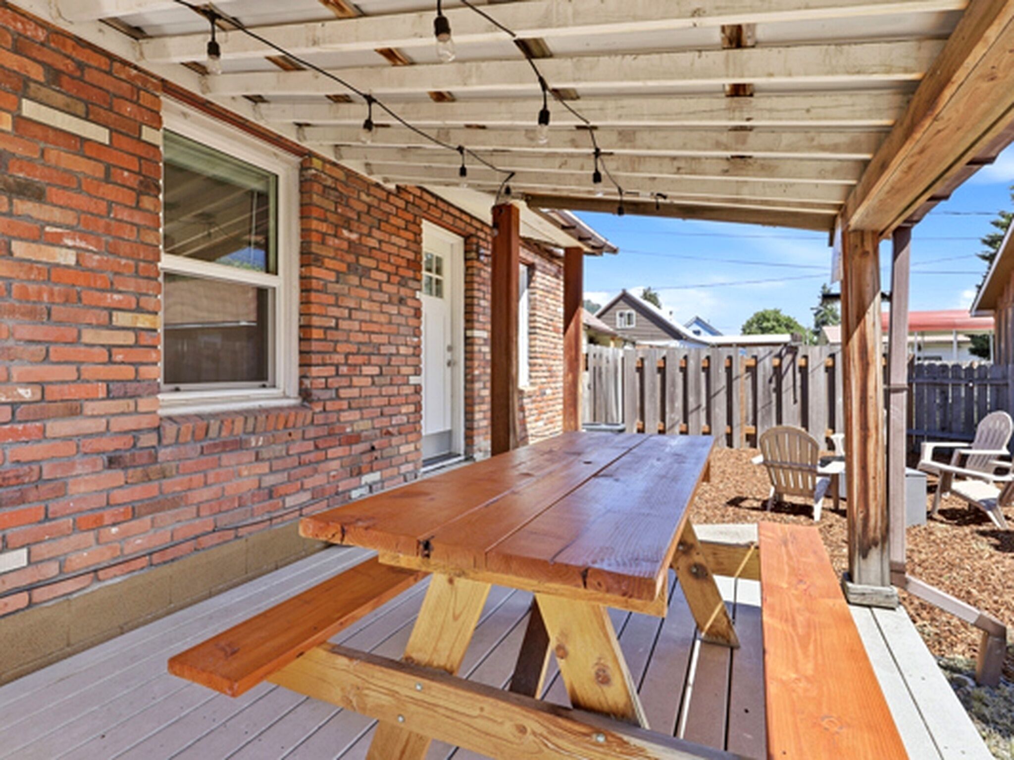 A wooden deck with a picnic table and chairs, a brick wall, and a covered area with string lights.