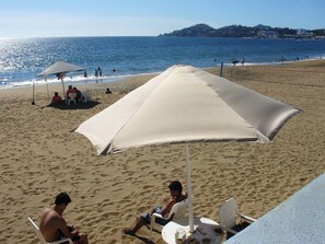 A beach with a large umbrella providing shade, a sandy beach, and a view of the sea. - APARTMENT IN THE HEART OF MANZANILLO, COLIMA (Manzanillo)