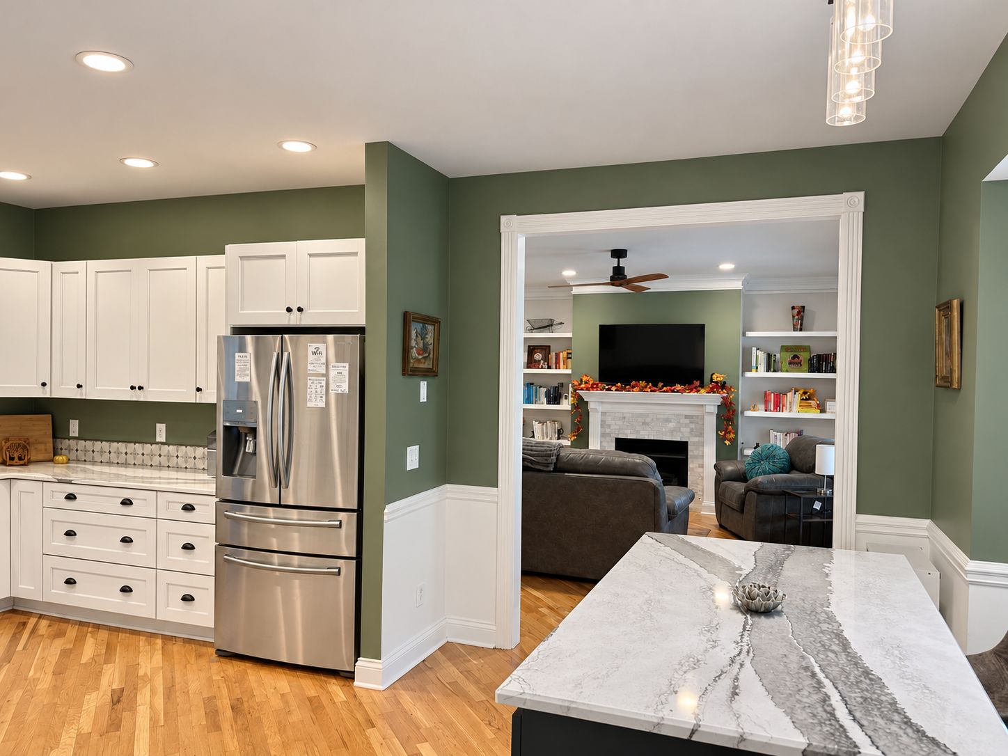 A modern kitchen with white cabinetry, a stainless steel refrigerator, and a marble island.