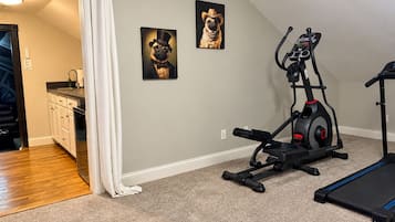 Un gimnasio en casa con equipo de ejercicio, una zona de cocina y dos cuadros en la pared.