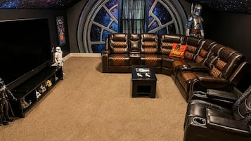 Um quarto com teto arredondado, uma janela ampla, um sofá de couro, uma mesa de centro e uma televisão.