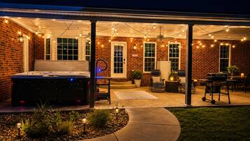 A covered patio area with a hot tub, seating, and string lights.