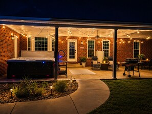 A covered patio area with a hot tub, seating, and string lights. - Country Getaway with Private Hot Tub, Pool, Game Rooms, & Star Wars Theater! (Portland)