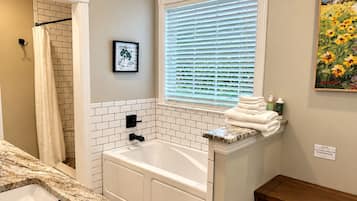 A bathroom with a bathtub, a sink, a window with blinds, a towel rack, and a painting on the wall.