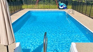 Una piscina rectangular con una escalera metálica, rodeada por una cerca y un tobogán al fondo.