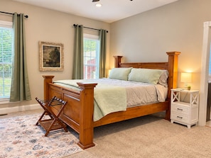 A bedroom with a wooden bed, a nightstand, a lamp, and a window with curtains.
