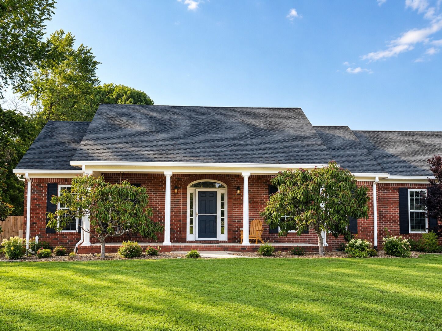 A two-story brick house with a front porch, a dark roof, and a well-maintained lawn.