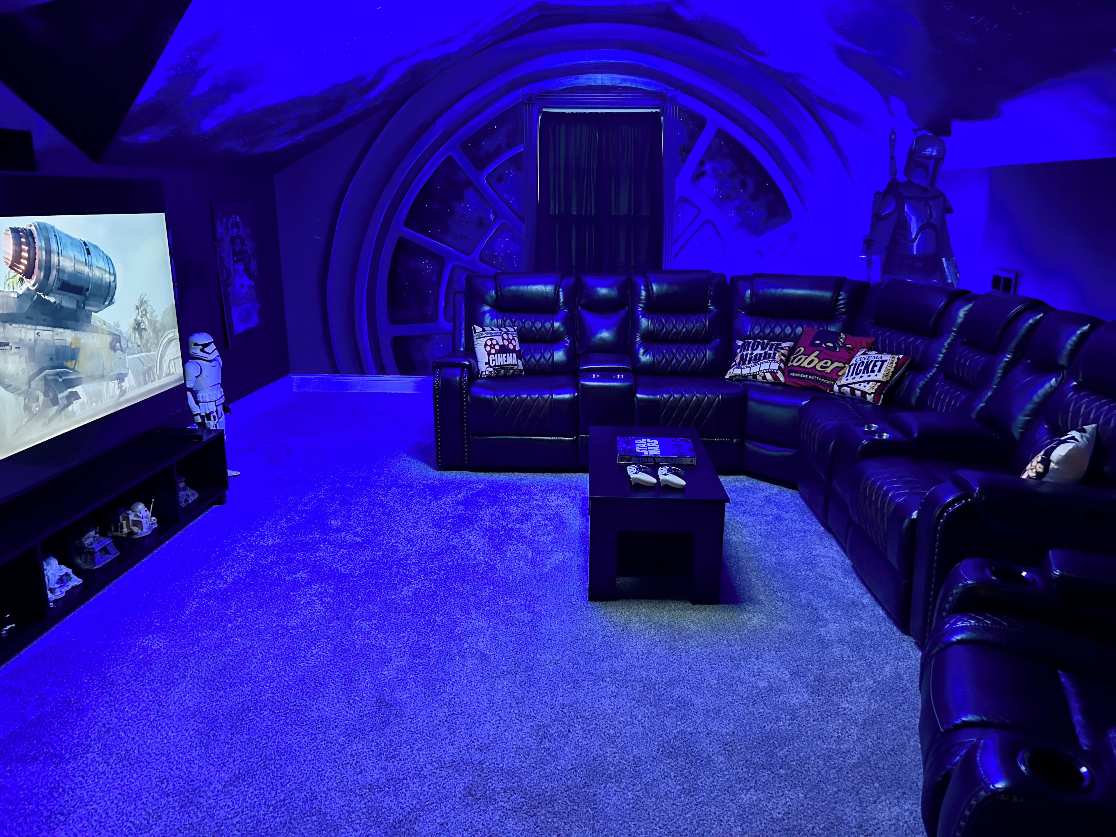 A room with a curved ceiling, a large screen, leather seating, and a Star Wars figure.