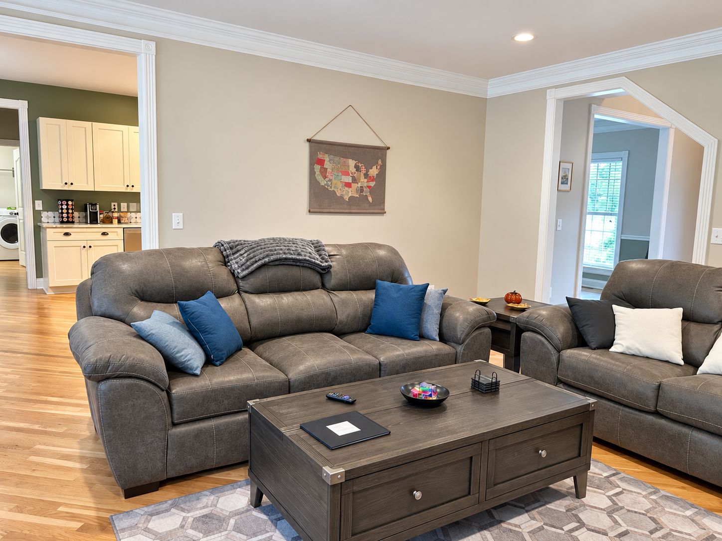 A living room with a grey leather sofa, a coffee table, and a map of the USA on the wall.