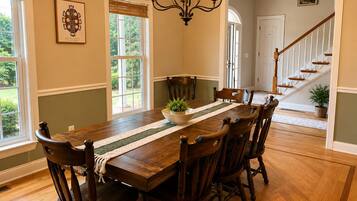 A dining room with a wooden table, chairs, a chandelier, and a view of a staircase.