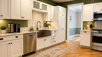 A kitchen with white cabinets, stainless steel appliances, a coffee maker, and a rug.