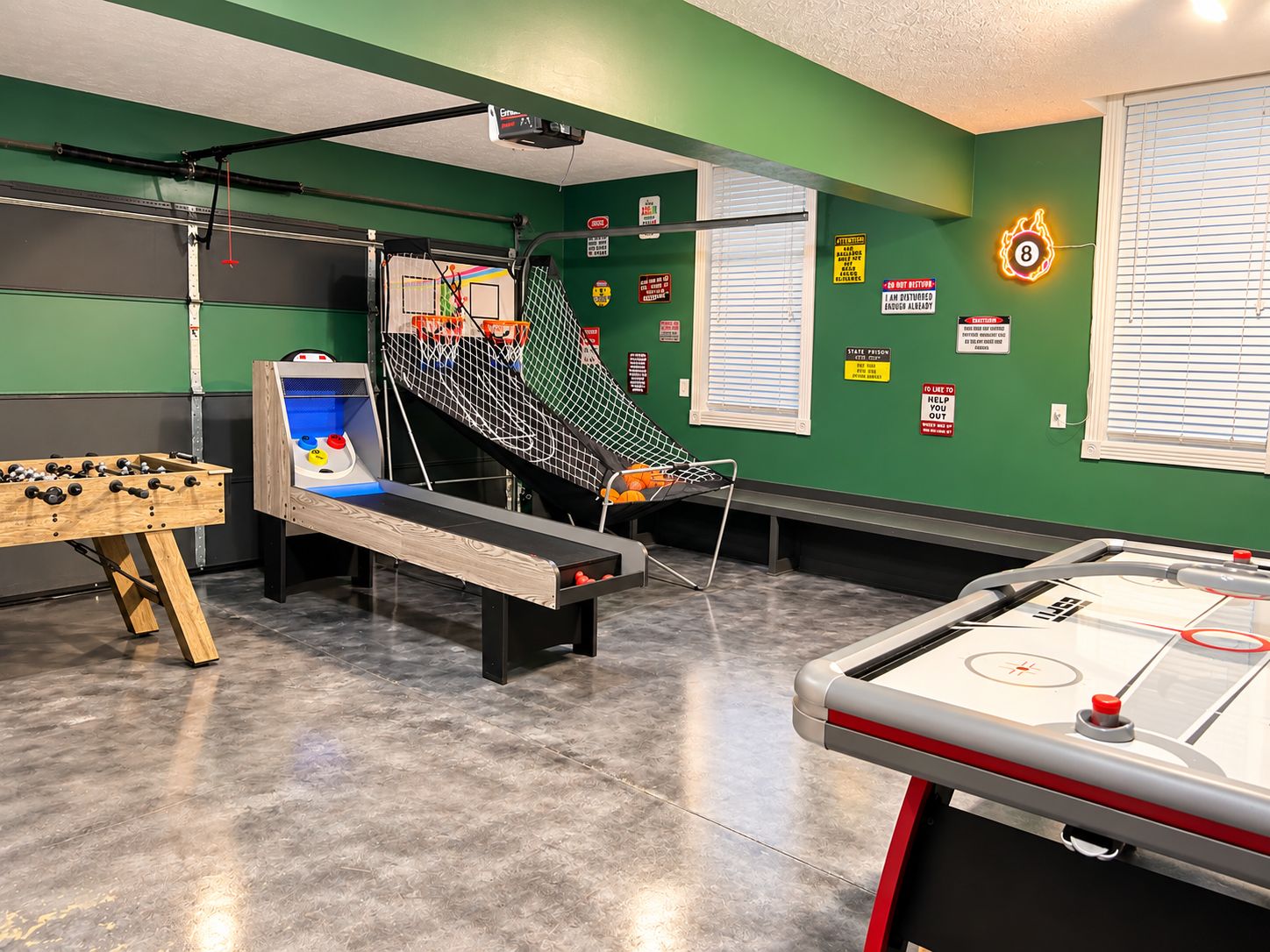 A recreational room with a foosball table, a shuffleboard table, and a small basketball hoop.