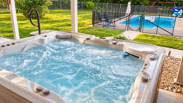 Jacuzzi con piscina al fondo, rodeado por una zona vallada con sillas y un tobogán.