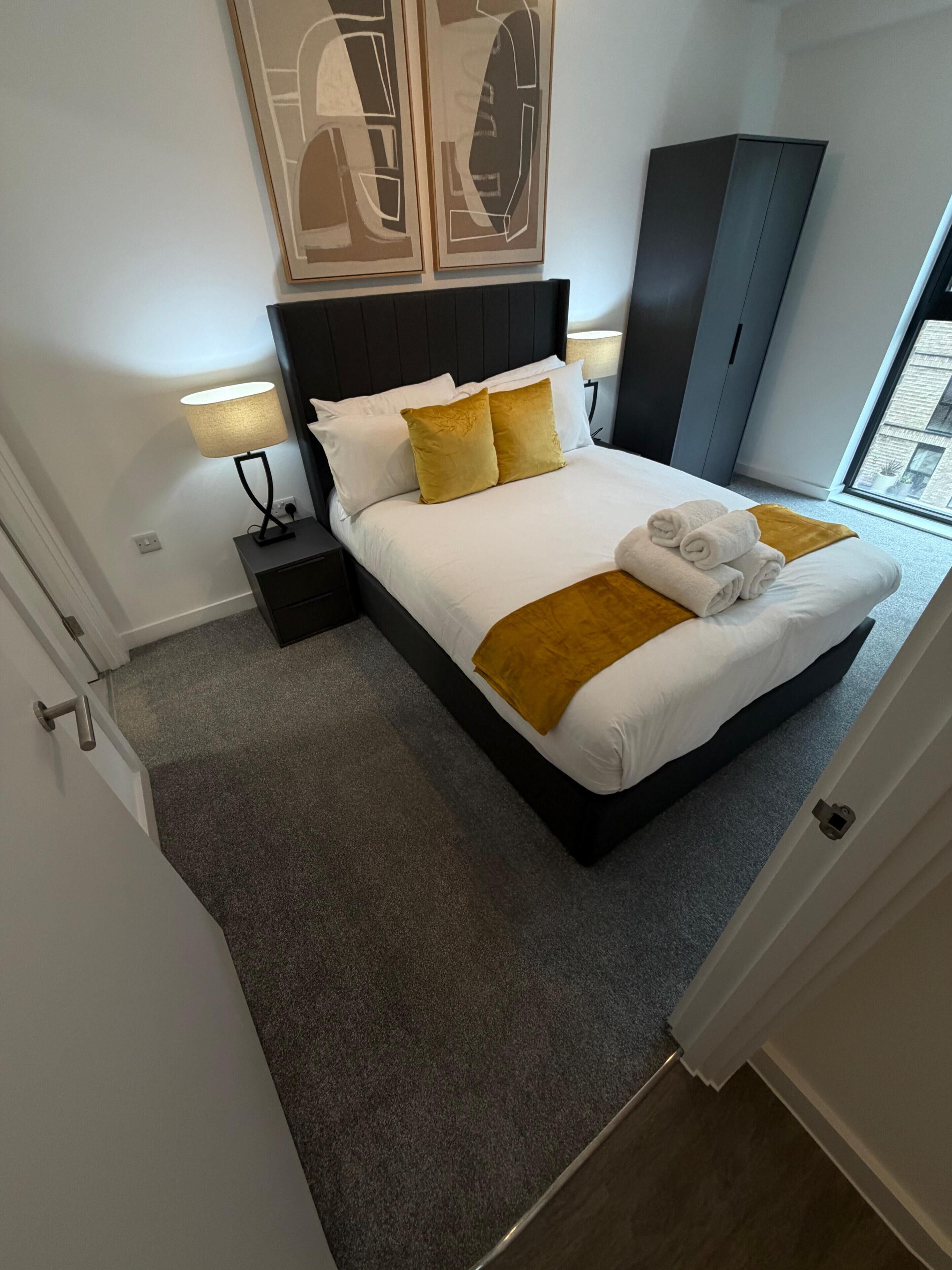 Ein ordentlich eingerichtetes Hotelzimmer mit einem Bett, einem Kleiderschrank, einem Nachttisch, einer Lampe und einem Fenster.