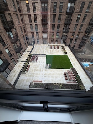 Un immeuble de grande hauteur doté d’un jardin sur le toit, comprenant des espaces aménagés pour s’asseoir et une petite pelouse.