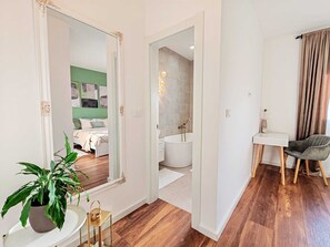 Ein modernes Hotelzimmer mit großem Spiegel, einem Bett, einem Badezimmer mit Badewanne und einem Schreibtisch mit Stuhl.