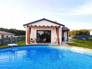Ein Wohnpool mit überdachter Terrasse, einem eingezäunten Garten und einem Haus im Hintergrund.