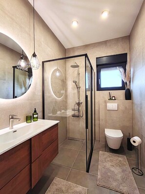 Ein modernes Badezimmer mit einer Glaskabine zur Dusche, einem großen Spiegel und einem Waschtisch mit Spüle und Stauraum.