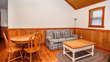 A room with a wooden dining table and chairs, a plaid sofa, and a small window with blinds.