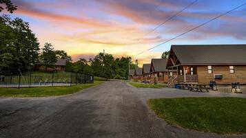 A campground with multiple cabins, a paved driveway, picnic tables, and a fenced playground area.